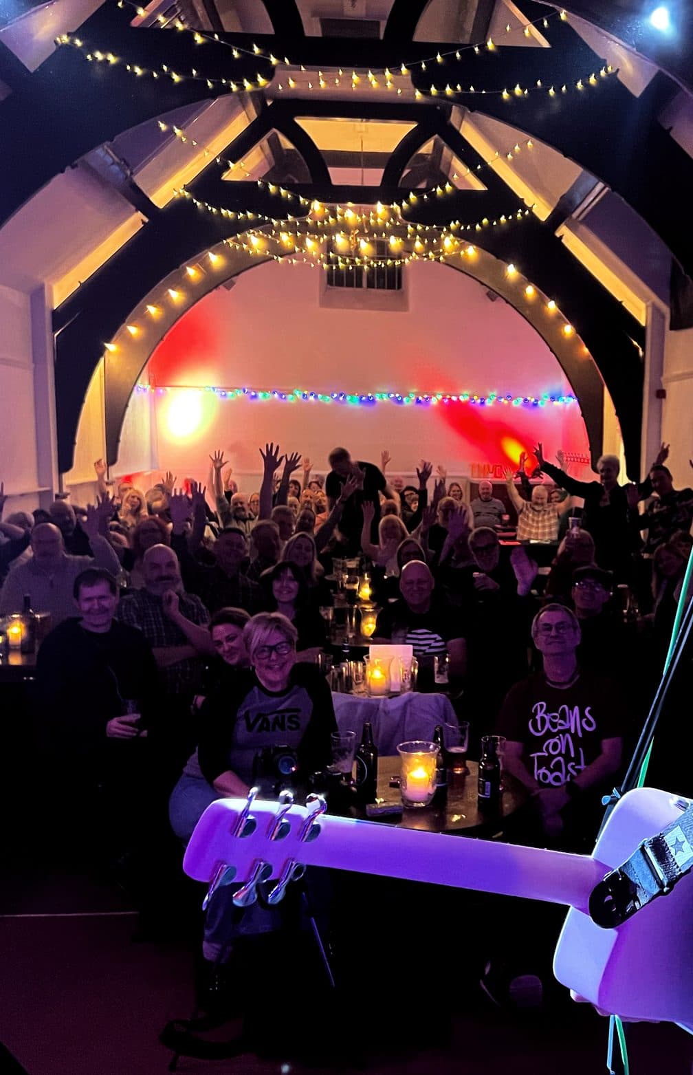 A full room at candlelit tables under the hall's arched roof, hands up for the band