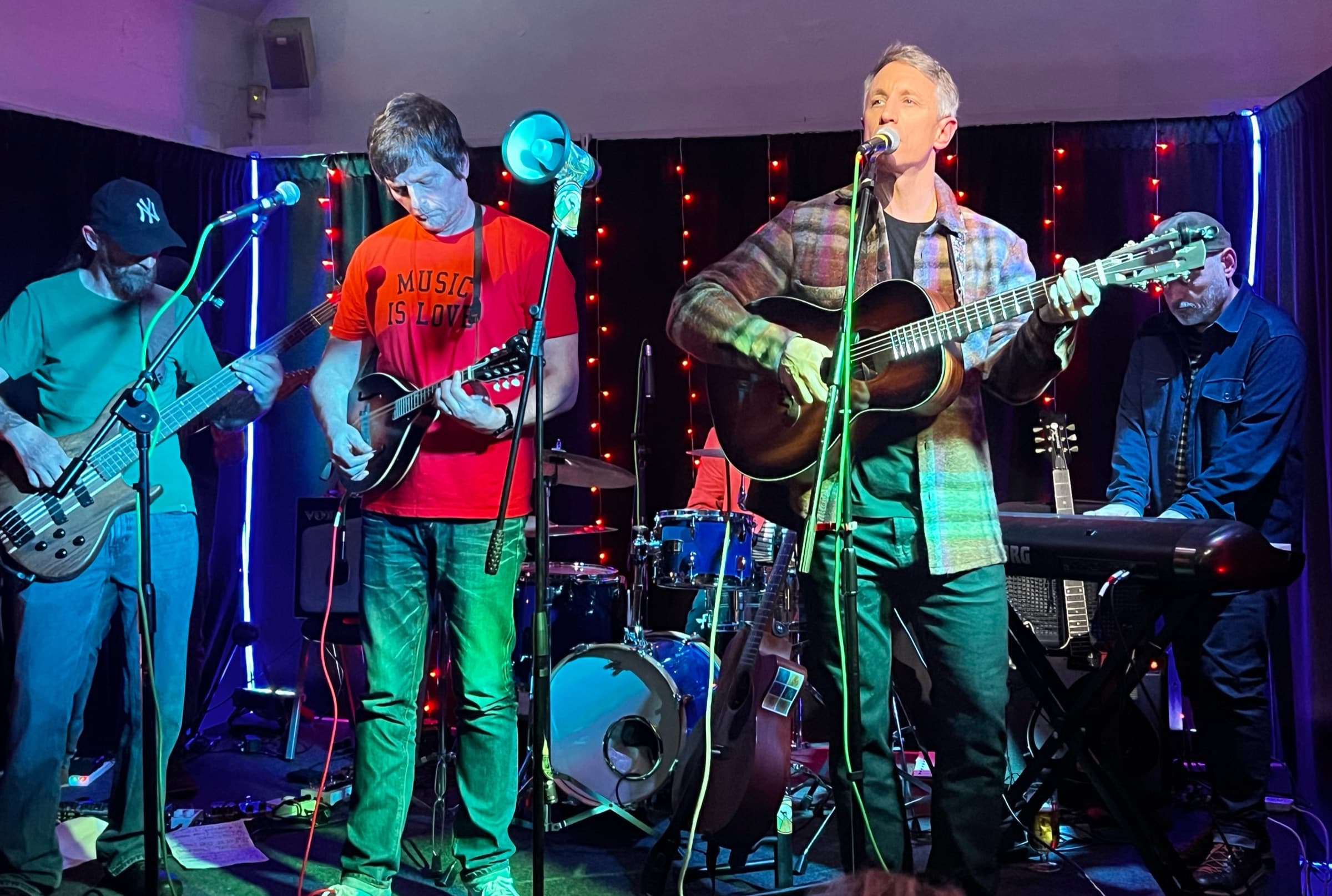 Professor Yaffle: a four-piece band on the stage under strings of red lights: bass, two guitars and keys