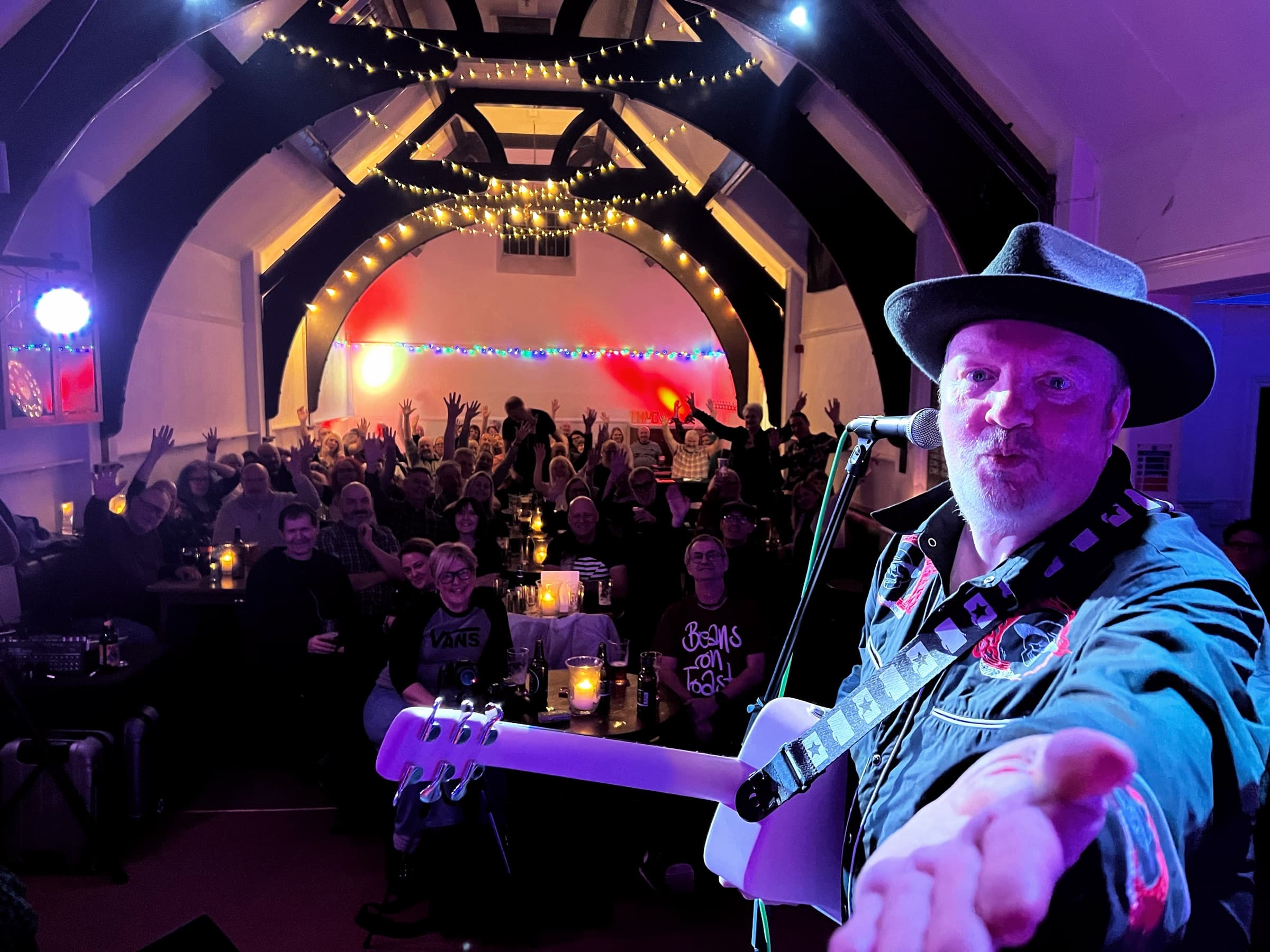 Pete Wylie: a singer in a black hat reaching toward the camera from the stage, the full room behind