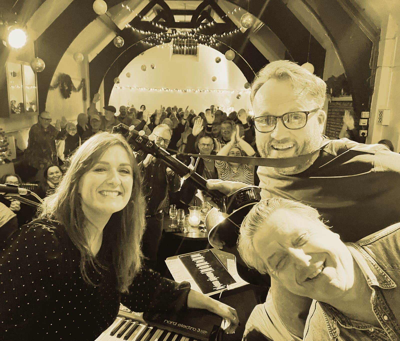Robert Vincent: three musicians at the keyboard smiling for a selfie, the room full behind them